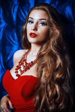 Beautiful woman with evening make-up and magnificent long hair wearing red dress.の写真素材