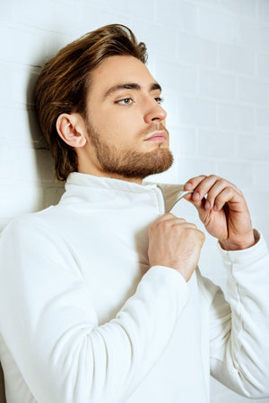 Beauty portrait of a handsome pensive young man standing by a white brick wall.の写真素材
