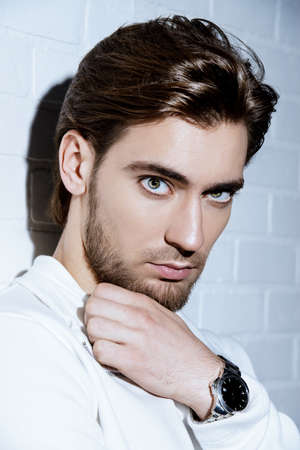 Beauty portrait of a handsome pensive young man standing by a white brick wall.の写真素材