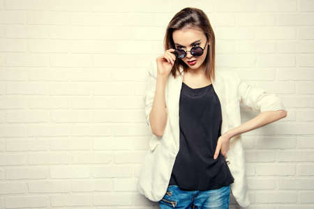 Modern brunette young woman in sunglasses posing by a white brick wall. Beauty, fashion. Youth style.の写真素材