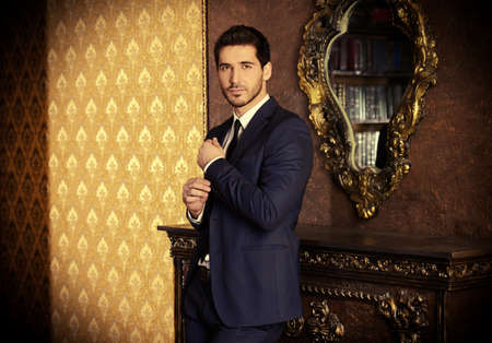 Respectable young man standing by a fireplace in a room with classic interior.の写真素材