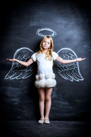 Cute child girl posing with angel wings drawn on a blackboard.の写真素材