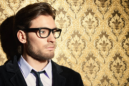 Portrait of a handsome young man standing by a golden vintage wallpaper.の写真素材