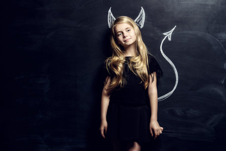 Cute child girl posing with imp horns and tail drawn on a blackboard.