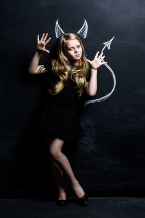 Cute child girl posing with imp horns and tail drawn on a blackboard.