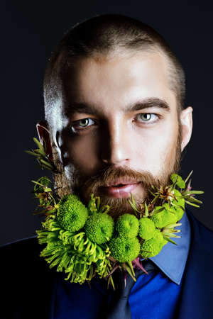 Portrait of a handsome man with a beard of green flowers. Men's beauty. Barbershop.の写真素材