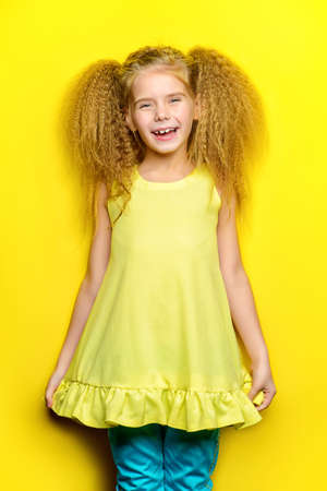 Joyful little girl with beautiful blonde hair over yellow background. Kid's style. Hairstyle.の写真素材