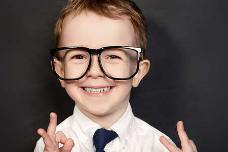 Four year old boy in white shirt and a tie posing by a school blackboard in big glasses. Educational concept.の写真素材
