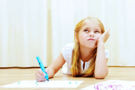 Cute girl lying on a floor and drawing on a paper with colorful pens.の写真素材