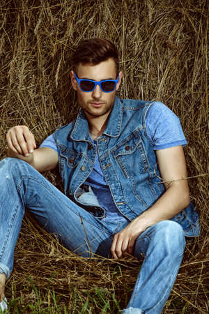 Handsome young man lying in haystack. Male fashion. Denim style.の写真素材