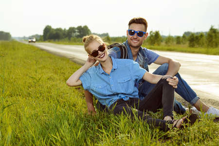 Hitchhiking couple. Happy young people sitting by the highway.の写真素材