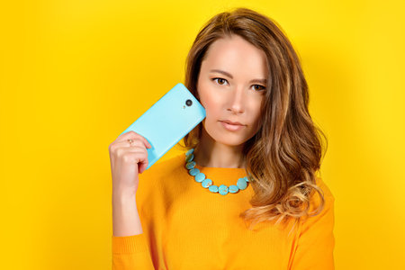 Smiling young woman posing with her  smartphone over yellow background. Beauty, fashion. Modern telecommunications.の写真素材