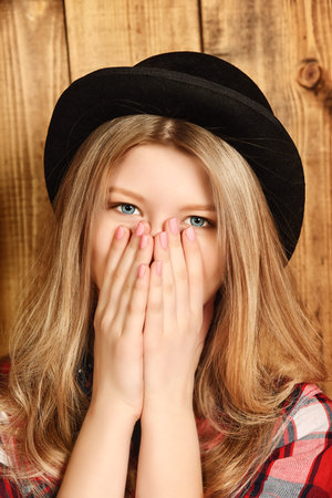 Pretty smiling girl wearing retro bowler hat over wooden background. Studio shot.の写真素材