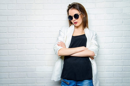 Modern brunette young woman in sunglasses posing by a white brick wall. Beauty, fashion. Youth...