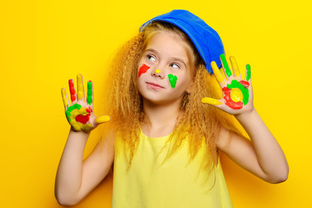 Cute laughing little girl with painted colorful hands over bright yellow background. Happy childhood.の写真素材