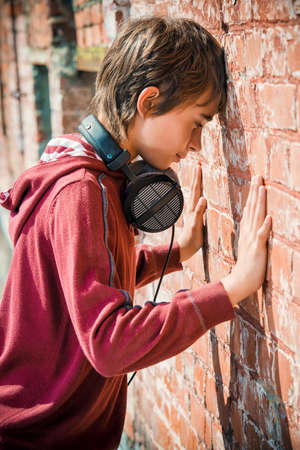 Teen boy standing in the street, turned away to face the wall. Sadness, depression. Teenage problems.の写真素材
