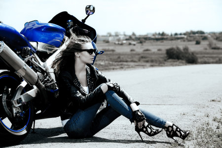 Black-and-white portrait of a beautiful biker woman sitting by her motorcycle on a highway. The spirit of freedom and independence.の写真素材