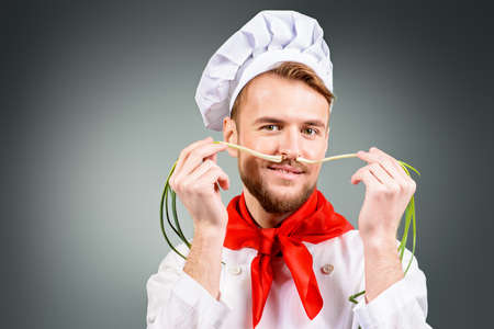 Smiling male cook holds a green onion as a mustache. Healthy eating. Copy space. Studio shot.の写真素材