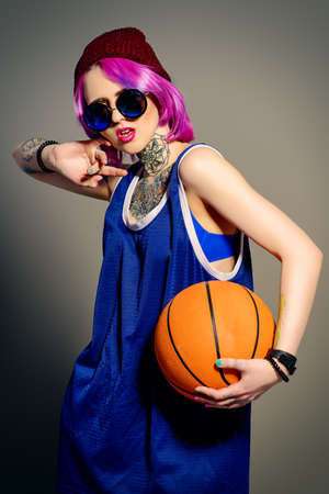 Style of modern youth. Bright girl in sports shirt holding basketball. Tattoo style. Hair coloring.の写真素材
