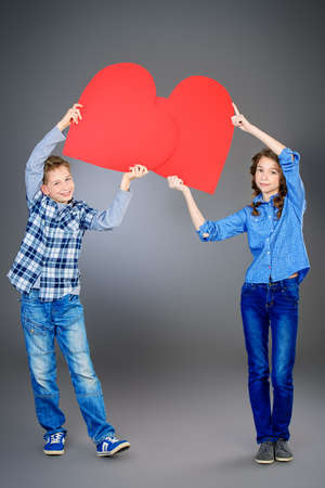 Two smiling teenagers standing together and holding red hearts. Valentine's day. Studio shot.の写真素材