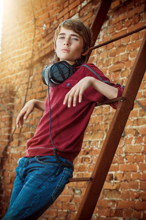 Modern teenage boy with headphones standing by a brick wall on the street. Modern generation. Summer holidays.の写真素材