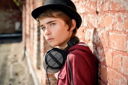 Teenage boy with headphones leaning to a brick wall on the street. Modern generation. Summer...