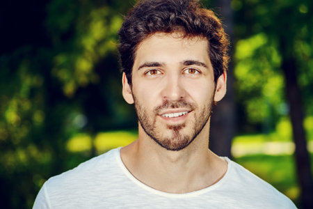 Smiling young man standing relaxed on a green lawn at a summer park.