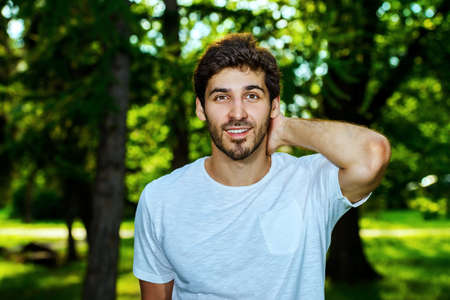 Smiling young man standing relaxed on a green lawn at a summer park.の写真素材