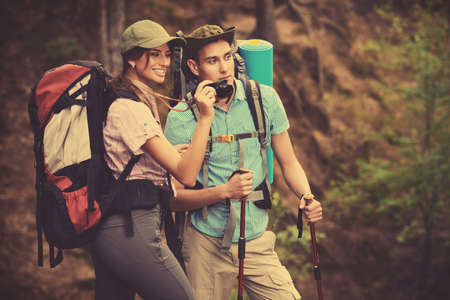 Hiking couple. Young people makes a hike in the woods. They take pictures of nature. Active lifestyle, tourism. Tourist equipment.の写真素材