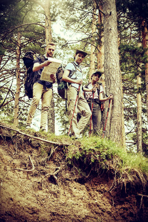Travelers group determines its location using the map. Hiking people in the wild forest. Adventure...