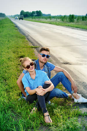Hitchhiking couple. Happy young people sitting by the highway.の写真素材