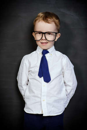 Four year old boy in white shirt and a tie posing by a school blackboard in big glasses. Educational concept.の写真素材