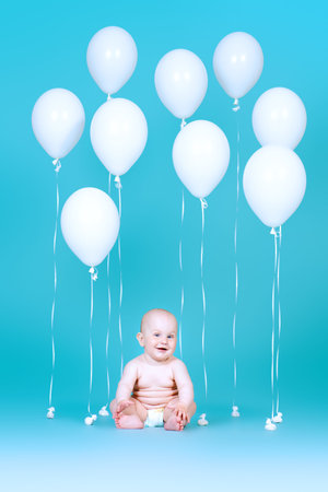 Adorable little baby sitting among white balloons over blue background. Infant baby. Healthcare....
