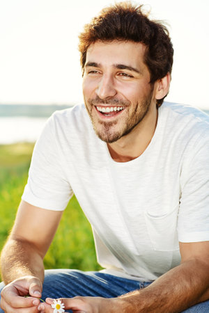 Handsome young man standing on a green lawn over urban background.の写真素材