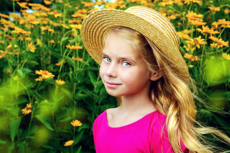 Portrait of a cute dreamy girl in a straw hat standing in a summer blooming park and smiling at camera. Happy childhood. Summer holidays.の写真素材