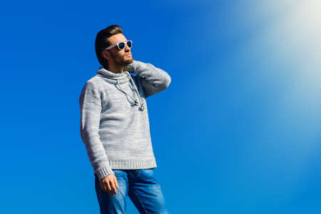 Young handsome man in casual clothes and sunglasses over blue sky. Men's beauty, fashion. Outdoor portrait.の写真素材