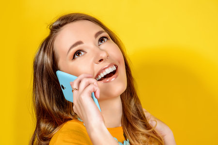 Smiling young woman posing with her  smartphone over yellow background. Beauty, fashion. Modern telecommunications.の写真素材