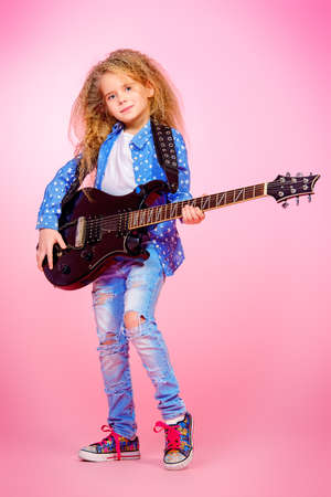 Modern seven year old girl with her electric guitar over pink background. Music concept.の写真素材