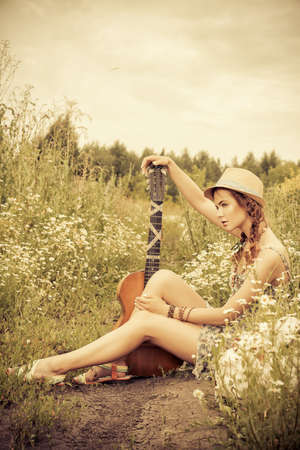 Beautiful romantic girl with a guitar on a country road on a sunny summer day.の写真素材