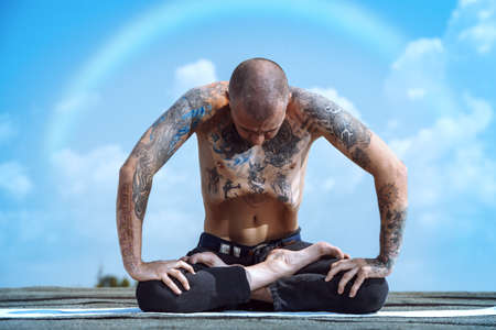 Yoga concept. Experienced yoga master meditates in the lotus position sitting on a roof over blue sky.の写真素材