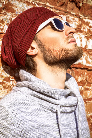 Handsome young man leaning against the brick wall on the street. Men's beauty, fashion.の写真素材