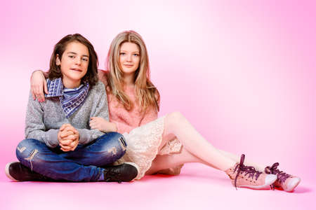 Happy teenage boy and girl sitting together over pink background. Friendship. First love.の写真素材