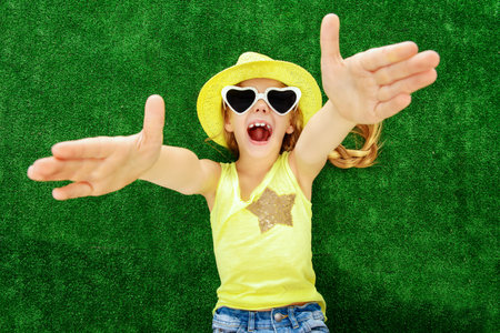 Joyful little girl in colorful clothes and sunglasses lying on a green lawn. Kid's fashion. Summer...