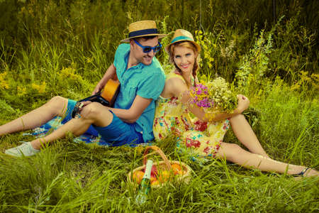 Enamored young man with a guitar singing his beloved girlfriend. They are sitting together on a lawn on a sunny summer day. Love concept.の写真素材