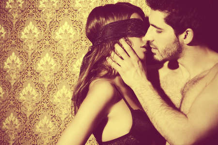 Sensual young woman with lace ribbon on her eyes and a handsome man kissing and playing in love games.の写真素材