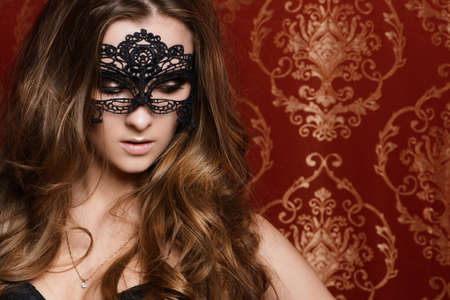 Beautiful young woman with long wavy hair wearing black lace mask. Carnival. Beauty, fashion.の写真素材