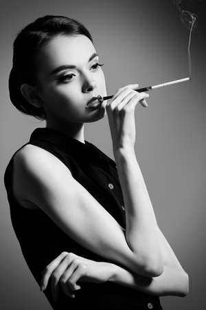 Fashion shot of an elegant brunette model smoking. Makeup and hair in the sixties style. Studio shot.の写真素材
