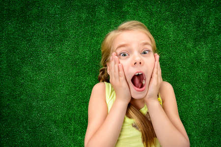 Funny little girl lying on a green lawn and expressing surprise. Kid's fashion. Summer holidays.の写真素材