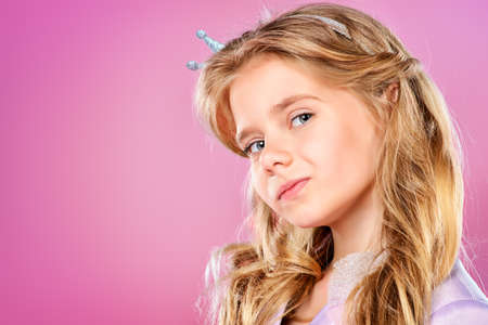 Portrait of a pretty little girl with beautiful blonde hair over pink background. Little princess with a crown on her head. Kids fashion.の写真素材