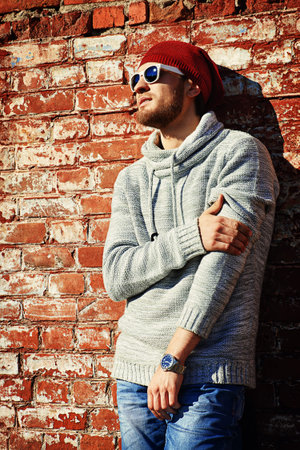 Handsome young man leaning against the brick wall on the street. Men's beauty, fashion.